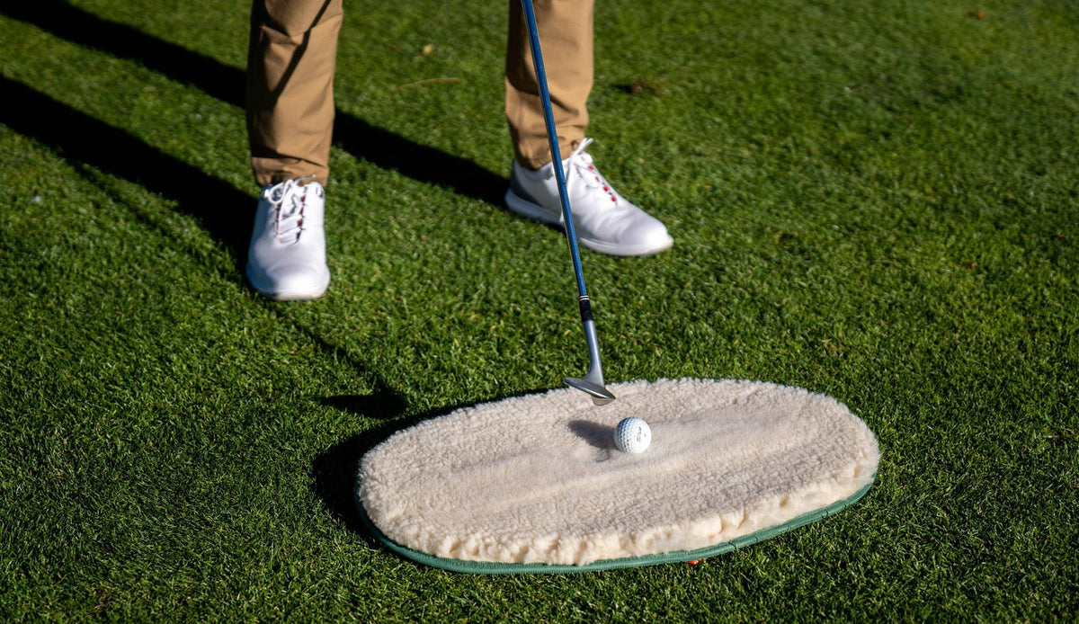 A golfer addressing a ball on the WhyGolf Bunker Mate, wedge resting on the fleece surface