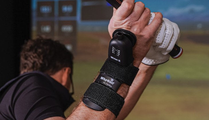 Golfer at the top of the backswing in a golf simulator wearing the Wrist-X wrist hinge trainer